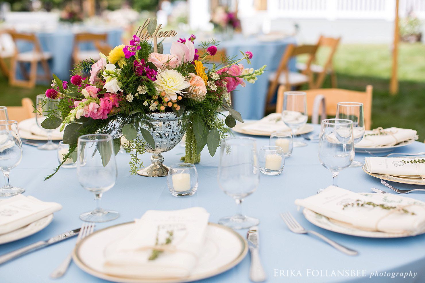 Colorful centerpieces on blue tablecloths with mismatched china plates